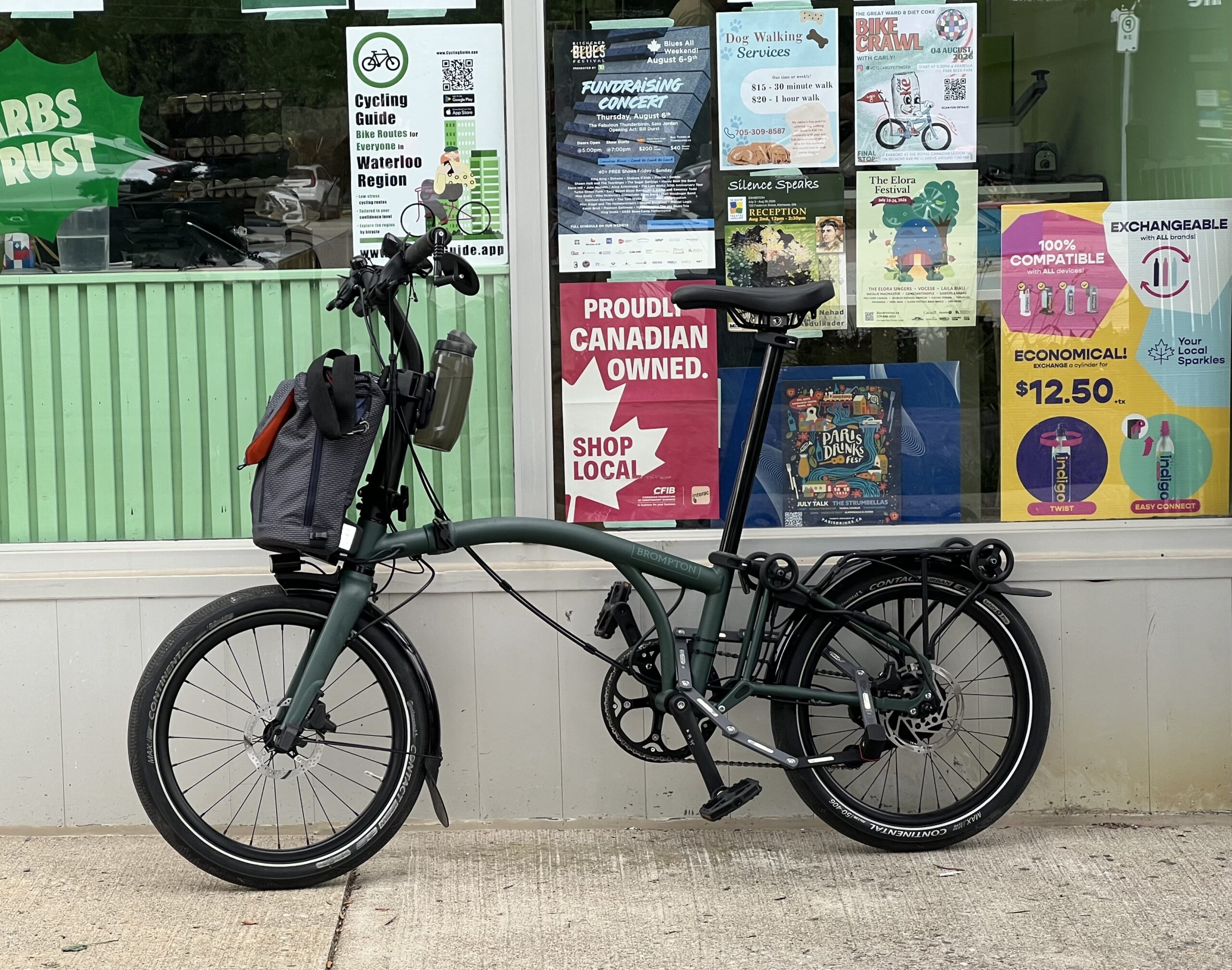 In the foreground, there’s a Brompton bicycle leaning against a storefront. Behind the Brompton in the store window, there are multiple posters, including one for Cycling Guide.