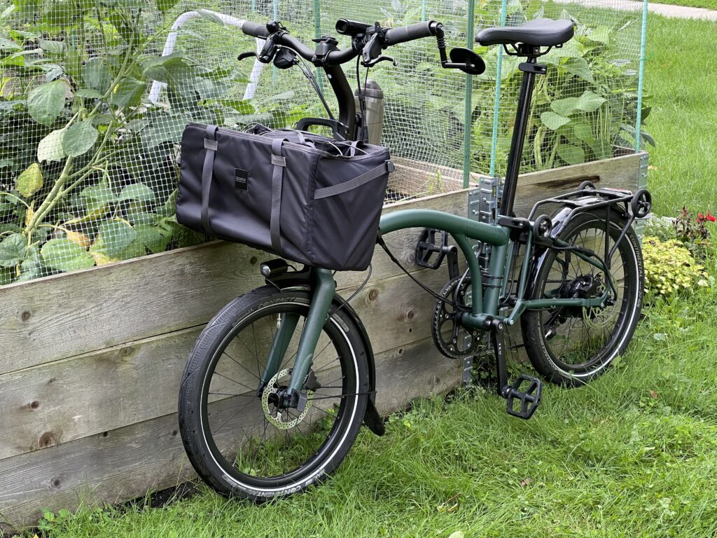 A three quarter front biew of a bike. There's a lrage bag hangng on the front. The bike is leaning against a raised vegatable garden bed..
